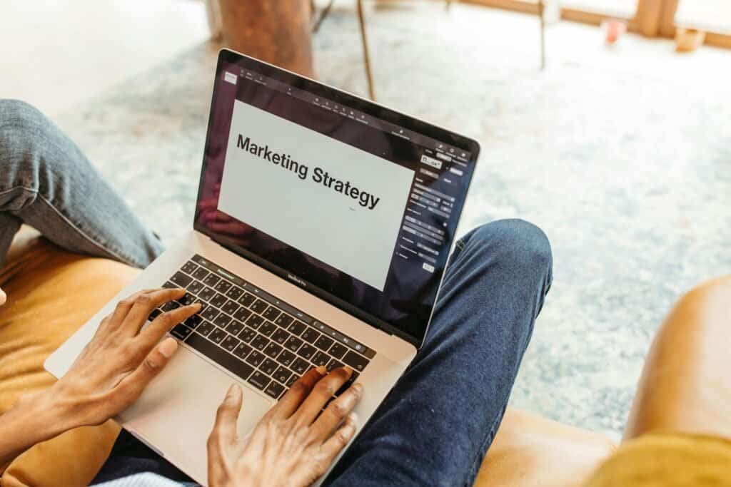 Two people using a laptop with the word marketing strategy on it.